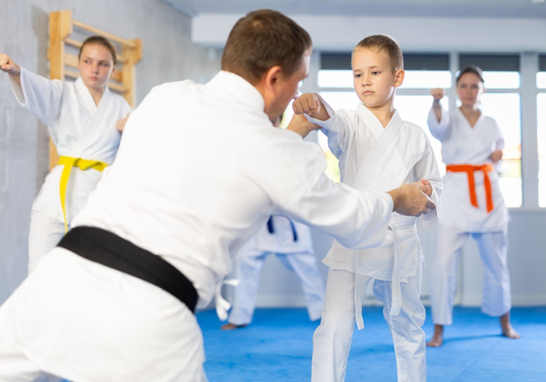 Boy train and learn during family group lesson in oriental martial arts. Man teacher corrects pose posture position of body, hands during karate classes.